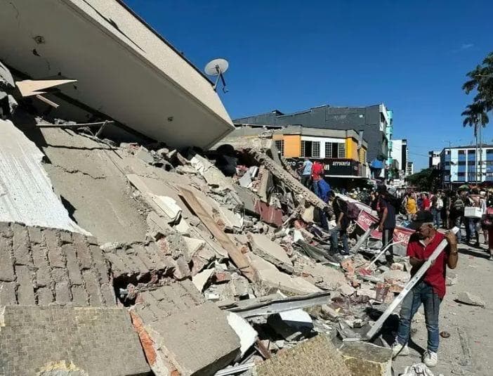 A collapsed building spilling concrete and brick rubble across a busy commercial street.